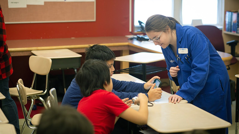 example of an outreach school program — bluecoat in the classroom speaking to two students at their desk