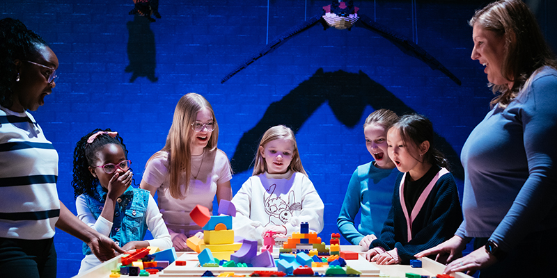 group of young girls laughing and playing with lego bricks with two bats made of lego bricks hanging above them