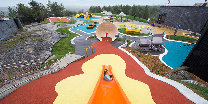 young girl sliding down slide at outdoor science park while another girl looks on